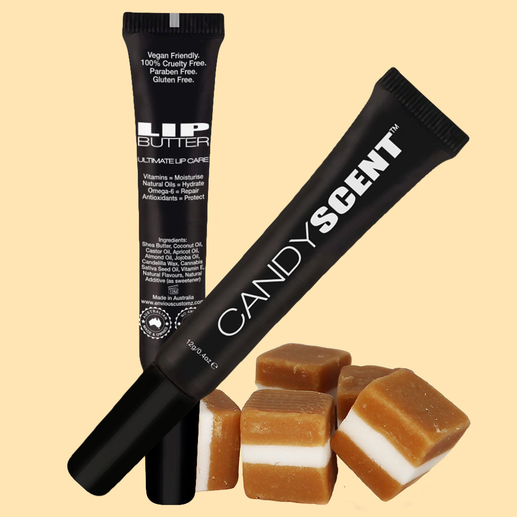 Two black tubes of lip care products are pictured, one labeled "Lip Butter" from the brand CANDYSCENT™. The Lip Butter tube highlights its use of natural ingredients and is vegan-friendly, cruelty-free, paraben-free, and gluten-free. Cubes of caramel candy are placed in front of the tubes.