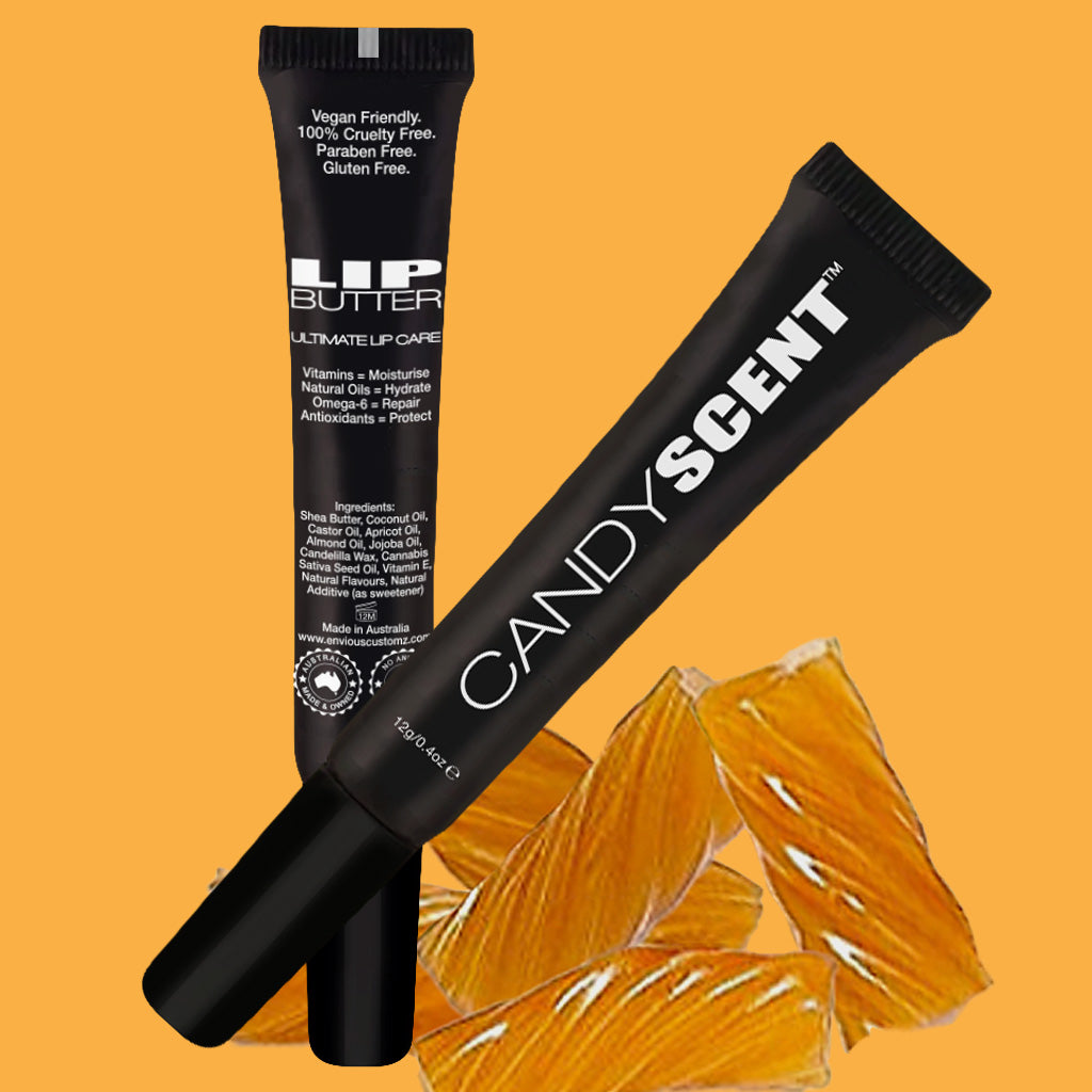Two tubes of lip balm from CANDYSCENT™ Lip Butter are placed against an orange background with images of candies. One tube lists benefits such as featuring natural ingredients, being vegan, cruelty-free, gluten-free, and packed with vitamins and antioxidants for moisturizing care.