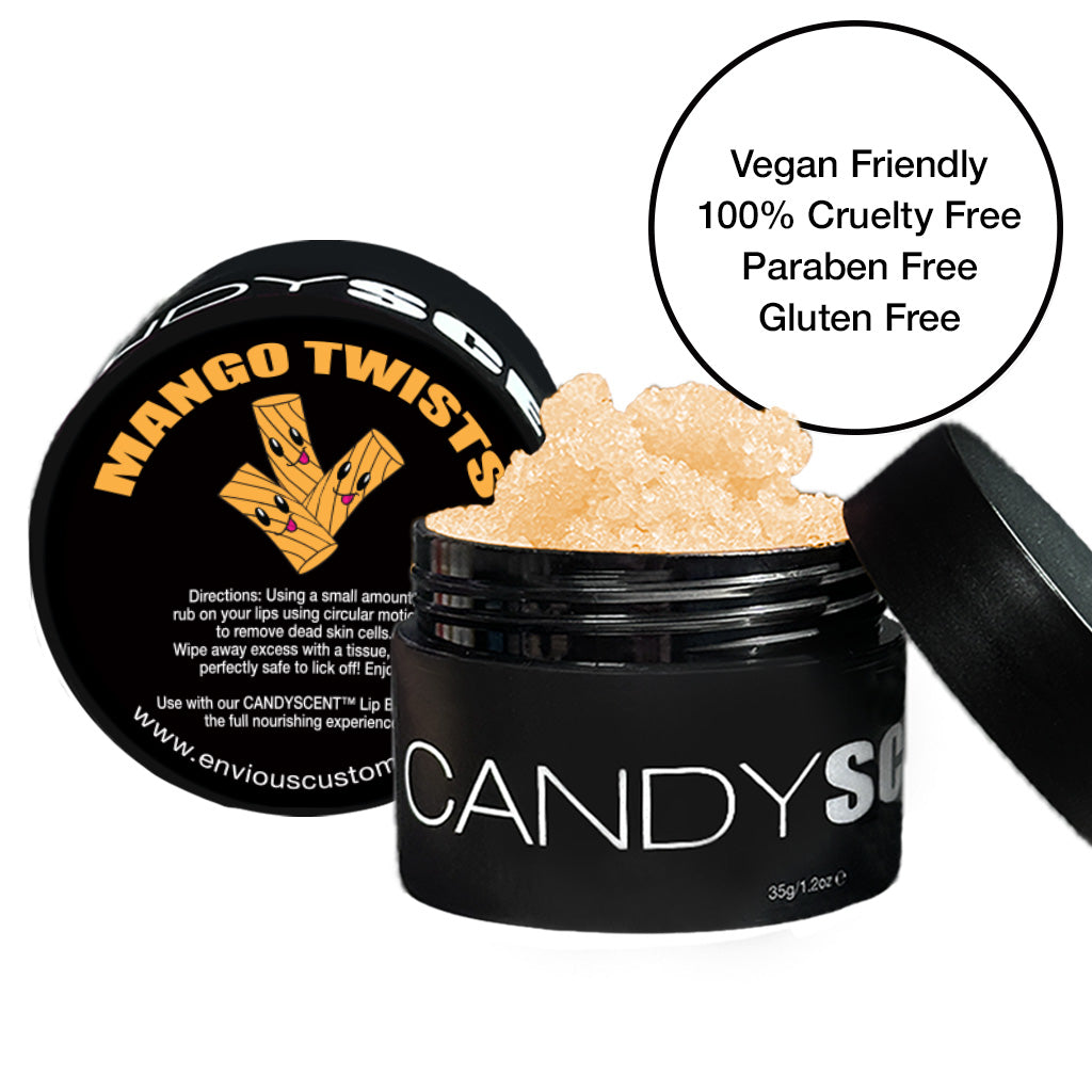 A black container labeled "CANDYSCENT™ Lip Sugar Scrub" with an open lid revealing a granular substance. The lid features the text "Mango Twists" and a graphic of mango slices. A circular label beside the container states "Vegan Friendly, 100% Cruelty Free, Paraben Free, Gluten Free." Perfect for exfoliating dead skin and enriched with nourishing oils.