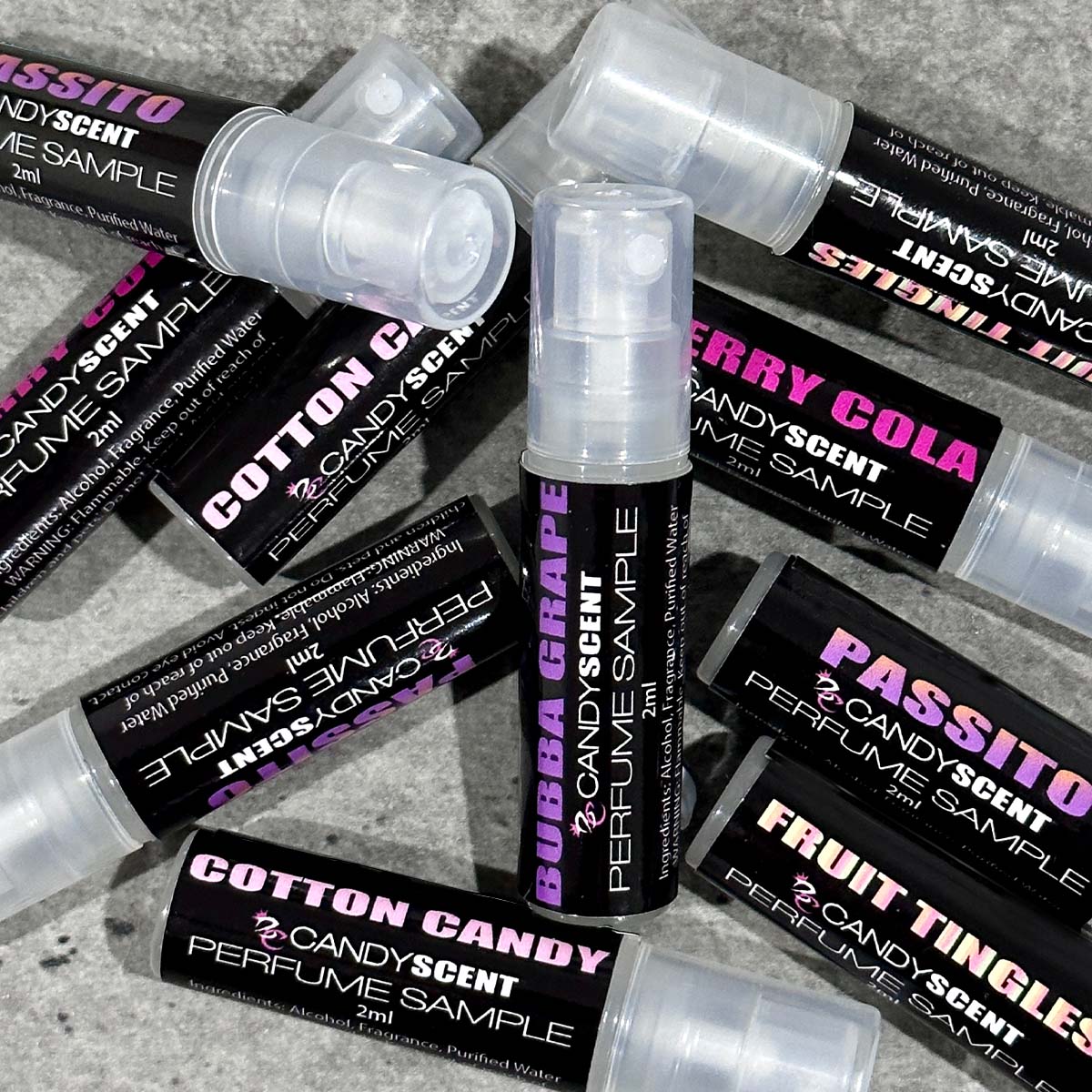 A scattered pile of CANDYSCENT™ Eau De Perfume / Cologne sample vials. Each vial has a black label with bright text highlighting various scents, such as