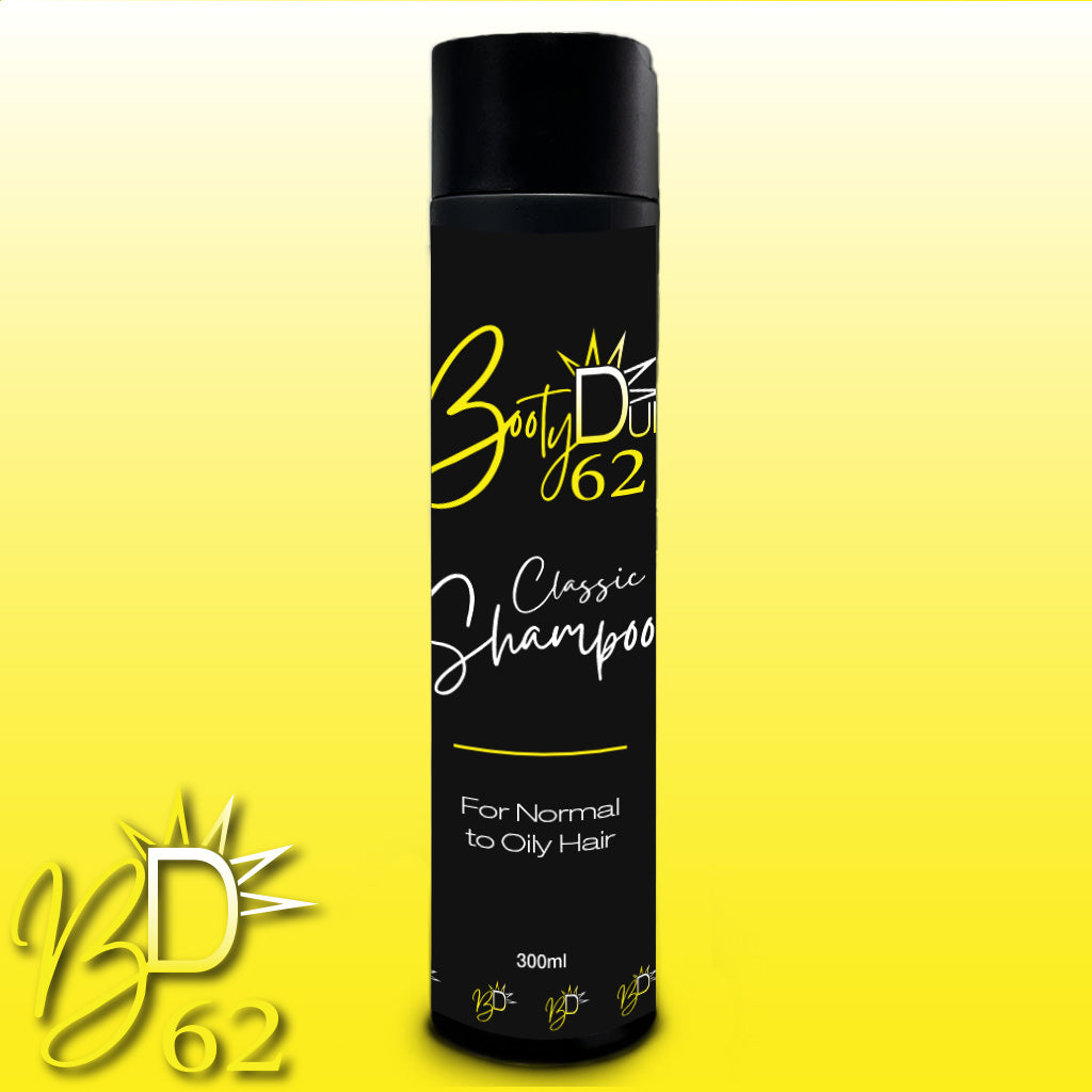 Image of a black and yellow bottle of BOOTY DUPE Classic Shampoo. The label reads "BOOTY DUPE, Classic Shampoo, For Normal to Oily Hair, 300ml." A stylized sunburst logo is present, and the background fades from white at the top to yellow at the bottom. It's an essential addition to your hair care routine to nourish your locks.