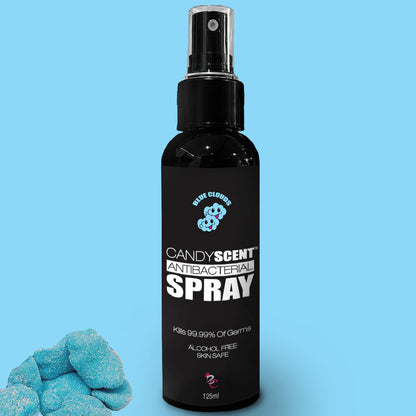 A black spray bottle labeled "Antibacterial Spray" from the CANDYSCENT™ brand, with a capacity of 125 ml, sits against a light blue background. The text highlights that the product kills 99.99% of germs, is alcohol-free, and safe for skin. Blue, cloud-shaped gummies adorn the bottom left corner.