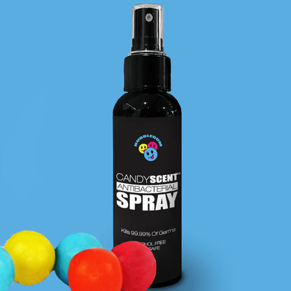 A black bottle of CANDYSCENT™ Antibacterial Spray featuring a smiling face logo on the label, set against a blue background. The alcohol-free spray, which kills 99.99% of germs, is highlighted by colorful gumdrop-like decorations positioned at the bottom left corner.