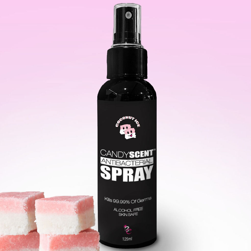 A black spray bottle labeled "CANDYSCENT™ Antibacterial Spray" in a Coconutted Candy scent against a gradient pink background. The alcohol-free bottle claims to kill 99.99% of germs and is skin-safe. Three pieces of pink and white candy are placed in front of the bottle.