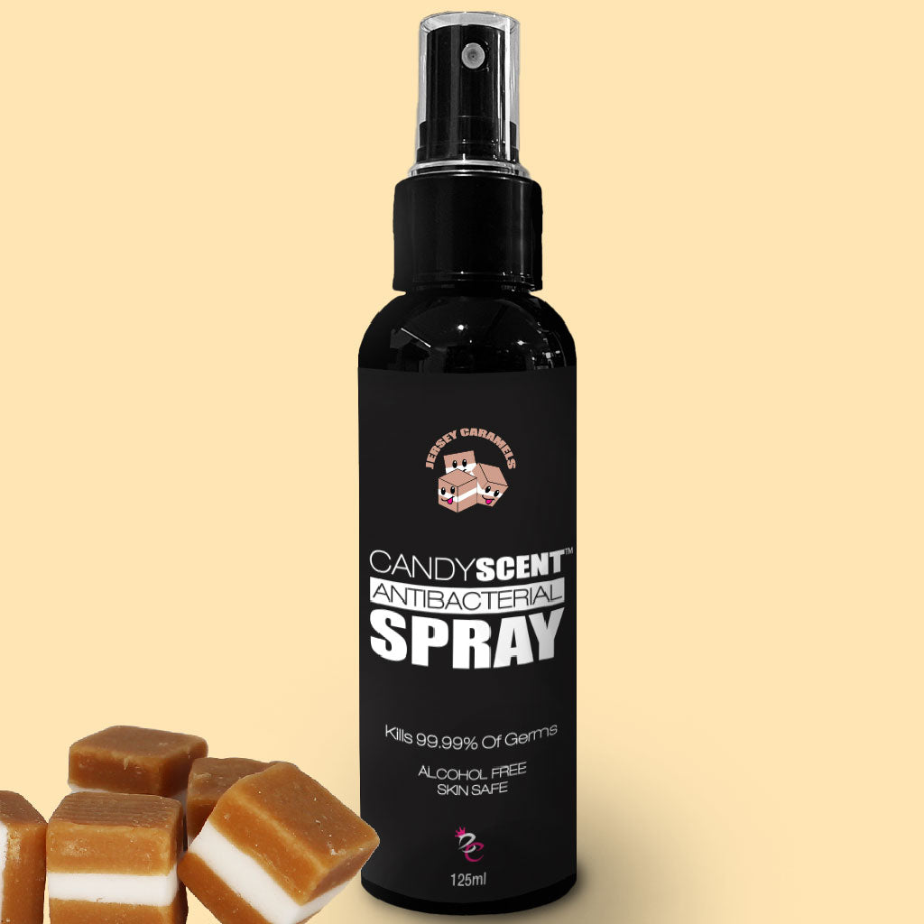 Image of a black spray bottle labeled "CANDYSCENT™ Antibacterial Spray" with a logo featuring two candy pieces. The text reads "Kills 99.99% of Germs," "Alcohol-Free," and "Skin Safe." Beside the antibacterial spray are caramel candy pieces with white layers. Quantity: 125ml.