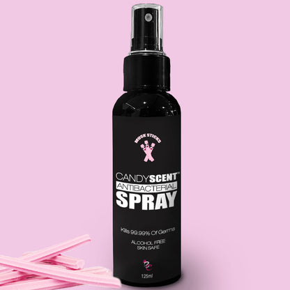 A black spray bottle labeled "Antibacterial Spray" by CANDYSCENT™ against a pink background. The bottle, adorned with the logos "Kink Sterz" and "NT," emphasizes that it kills 99.99% of germs, is alcohol-free, and skin-safe. Pink candy sticks are positioned beside the bottle.