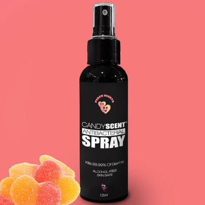 A 125ml bottle of CANDYSCENT™ Antibacterial Spray, featuring a "Fresh Hearts" logo and the text, "Kills 99.99% of Germs" and "Alcohol-Free, Skin Safe." The pink background showcases gummy heart candies on the left side.