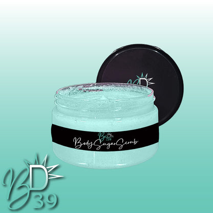 A jar of BOOTY DUPE Body Sugar Scrub for all skin types is shown with the lid open and placed behind the jar. The light blue scrub inside promises to exfoliate and hydrate. The BOOTY DUPE logo and the text "Body Sugar Scrub" are prominently displayed on the label. The background features a gradient of light blue to teal.