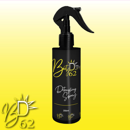 A black 200ml spray bottle of BOOTY DUPE’s Hair Detangling Spray with a trigger nozzle. The bottle features yellow and white labeling with a sunburst design, boasting Aloe Vera and Jojoba Oil for all hair types. The background is a gradient from white to yellow, with the "BD 62" logo at the bottom left corner.