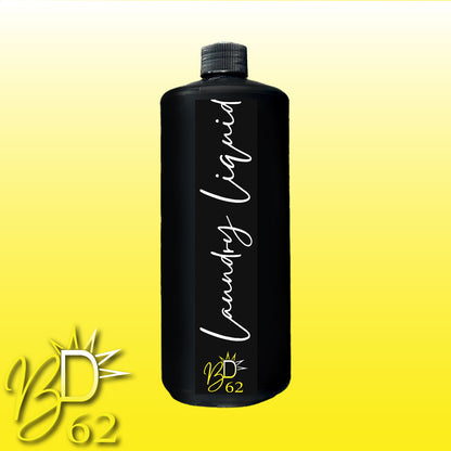 A black bottle of BOOTY DUPE Laundry Liquid with a handwritten white label reading "Laundry Liquid" stands out on a gradient yellow background. The lower left corner features the logo "BD 62" accompanied by a stylized sunburst design, promising long-lasting freshness and an eco-friendly formula.