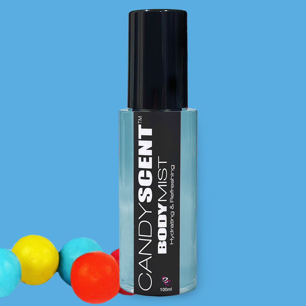 A bottle of CANDYSCENT™ Hydrating Body Mist labeled "Hydrating & Refreshing," is positioned against a blue background. The clear bottle, with a black spray cap and containing 100 ml of liquid, boasts nourishing ingredients like witch hazel. Colorful gumballs—yellow, red, and blue—are scattered at the base.