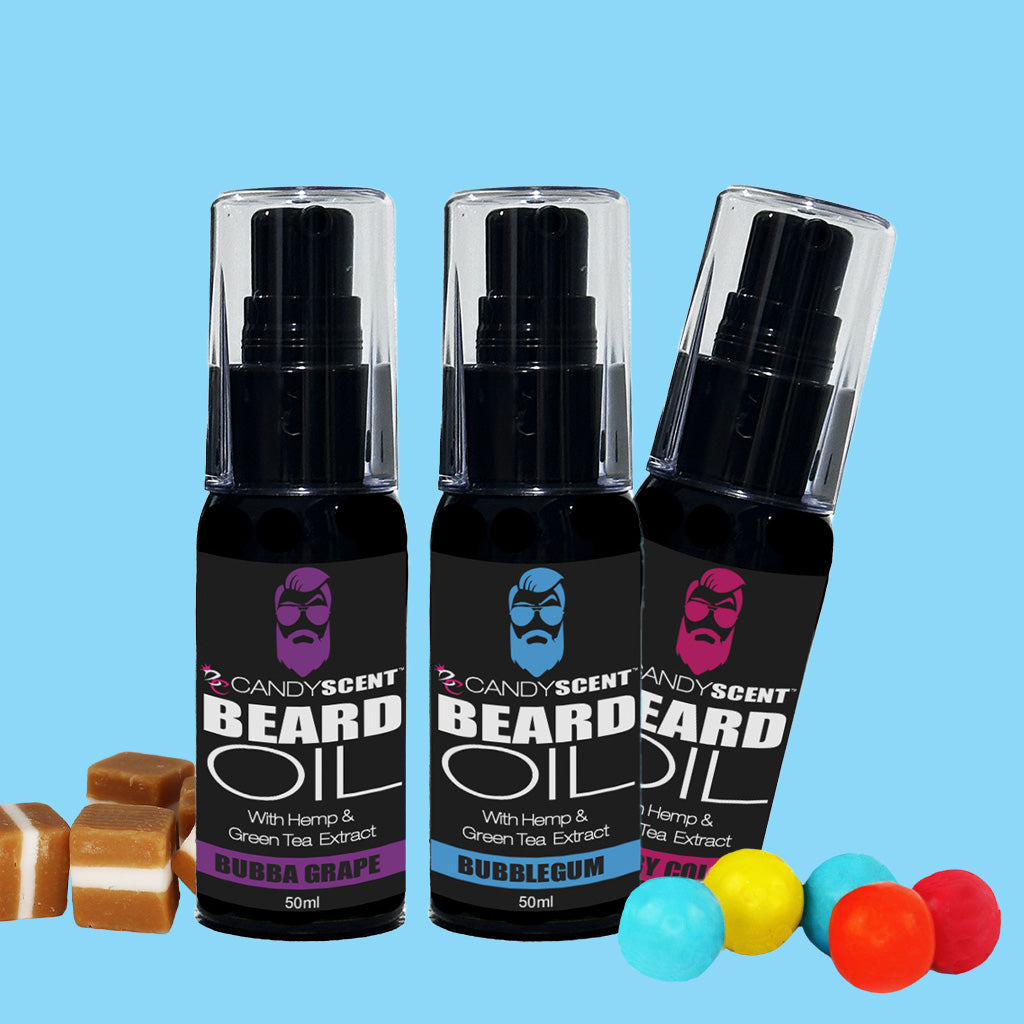 Three bottles of CANDYSCENT™ Beard Oil are showcased against a light blue background, each displaying designs for scents Bubble Grape, Bubblegum, and Caramel. Caramel candies are artfully arranged beside the Bubble Grape and Bubblegum bottles, with gumballs surrounding the Caramel bottle. Enhance your grooming routine with these enchanting scents that promote optimal beard health.