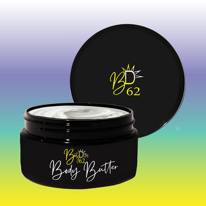 An open black jar of BOOTY DUPE's Triple Butter Body Butter, adorned with the "BD 62" logo on its lid, showcases the creamy formula that offers deep nourishment. The label elegantly displays "Body Butter" in cursive over a soothing gradient of pastel purple, blue, and green.