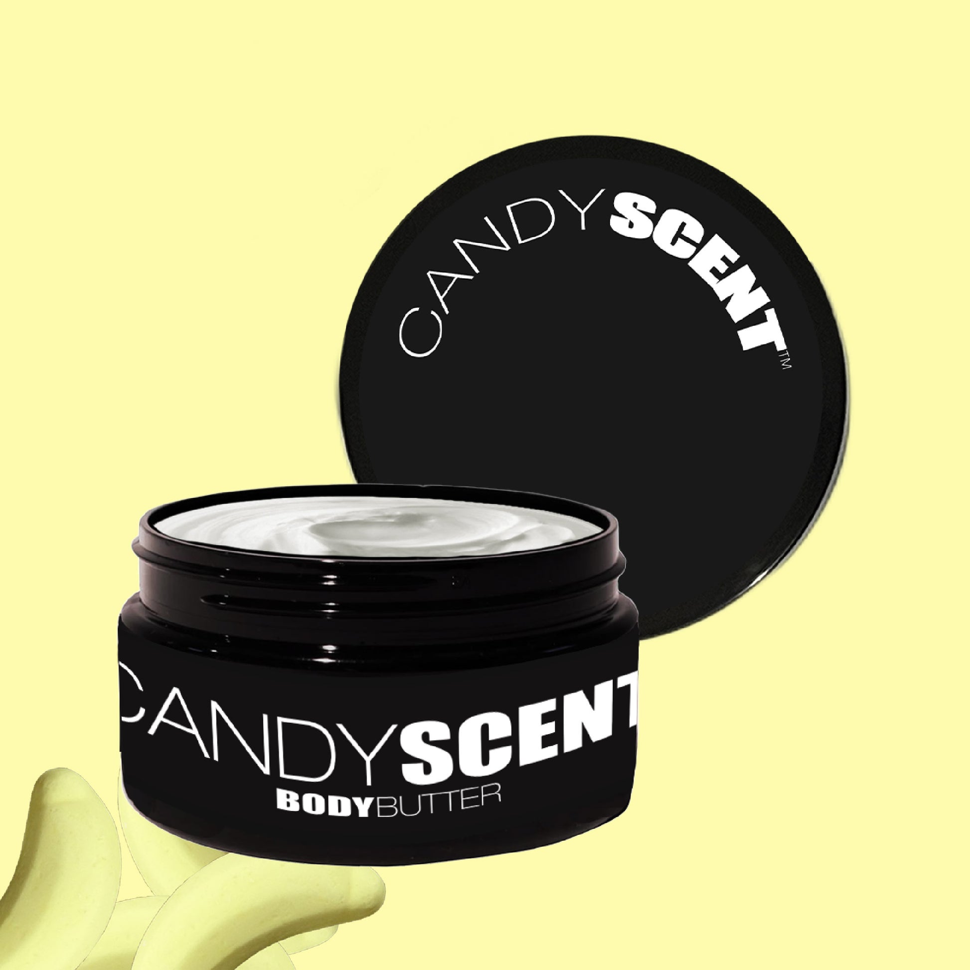 A black jar of CANDYSCENT™ Body Butter, partially open to showcase its creamy white content, promises intense nourishment. The light yellow background, adorned with subtle abstract shapes, enhances the luxurious appeal of this hydrating treat.