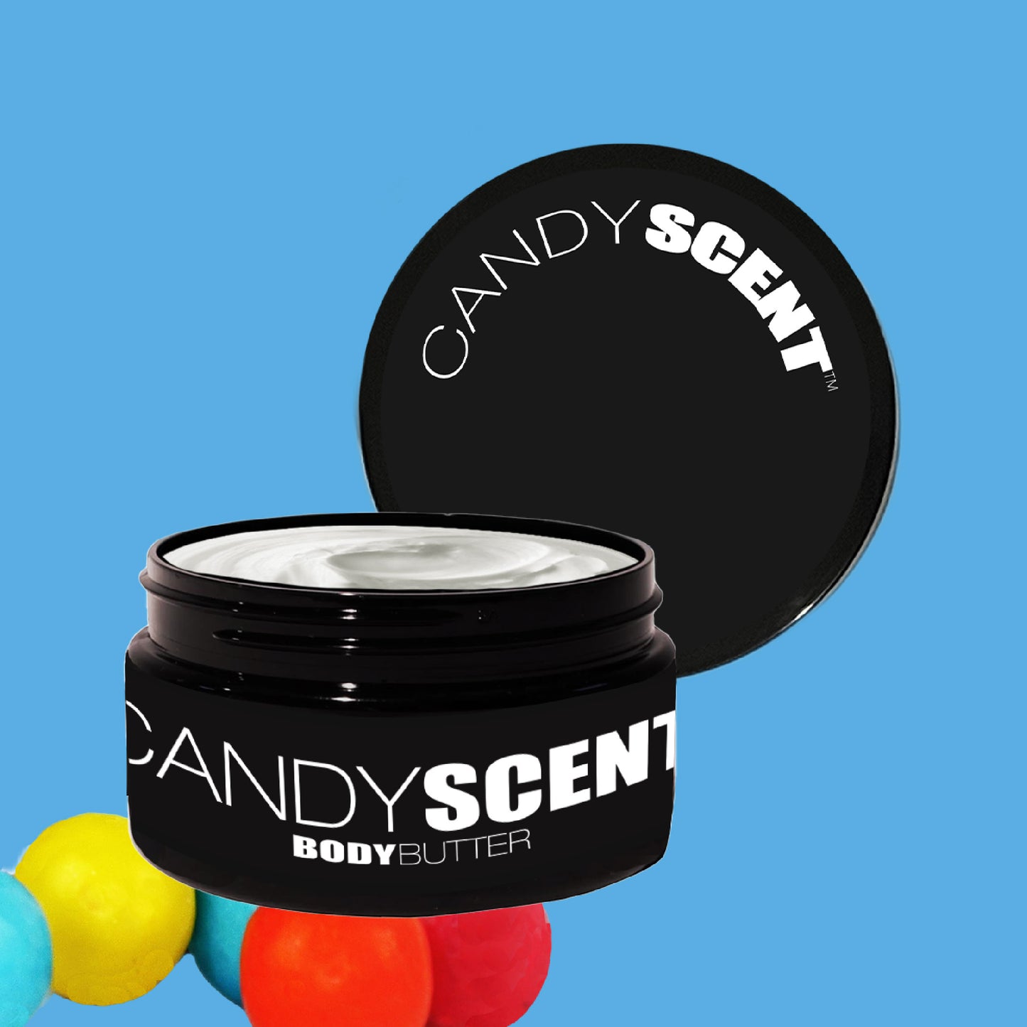 A black container of CANDYSCENT™ Body Butter is open, revealing its creamy texture ideal for hydration and nourishment. The lid, featuring the product name, rests against the container. A vibrant arrangement of colorful rubber balls lies at the bottom on a bright blue background.