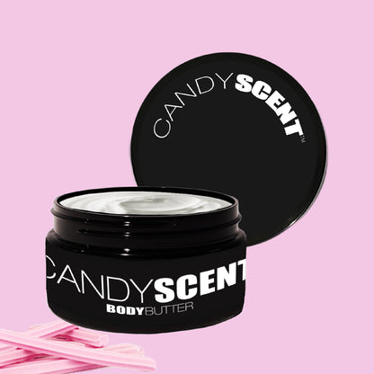 A black container of "Body Butter" from CANDYSCENT™ rests against a pink background. The open lid reveals nourishing white cream inside. Pink candy sticks are placed beside the jar, hinting at the hydrating treat within.