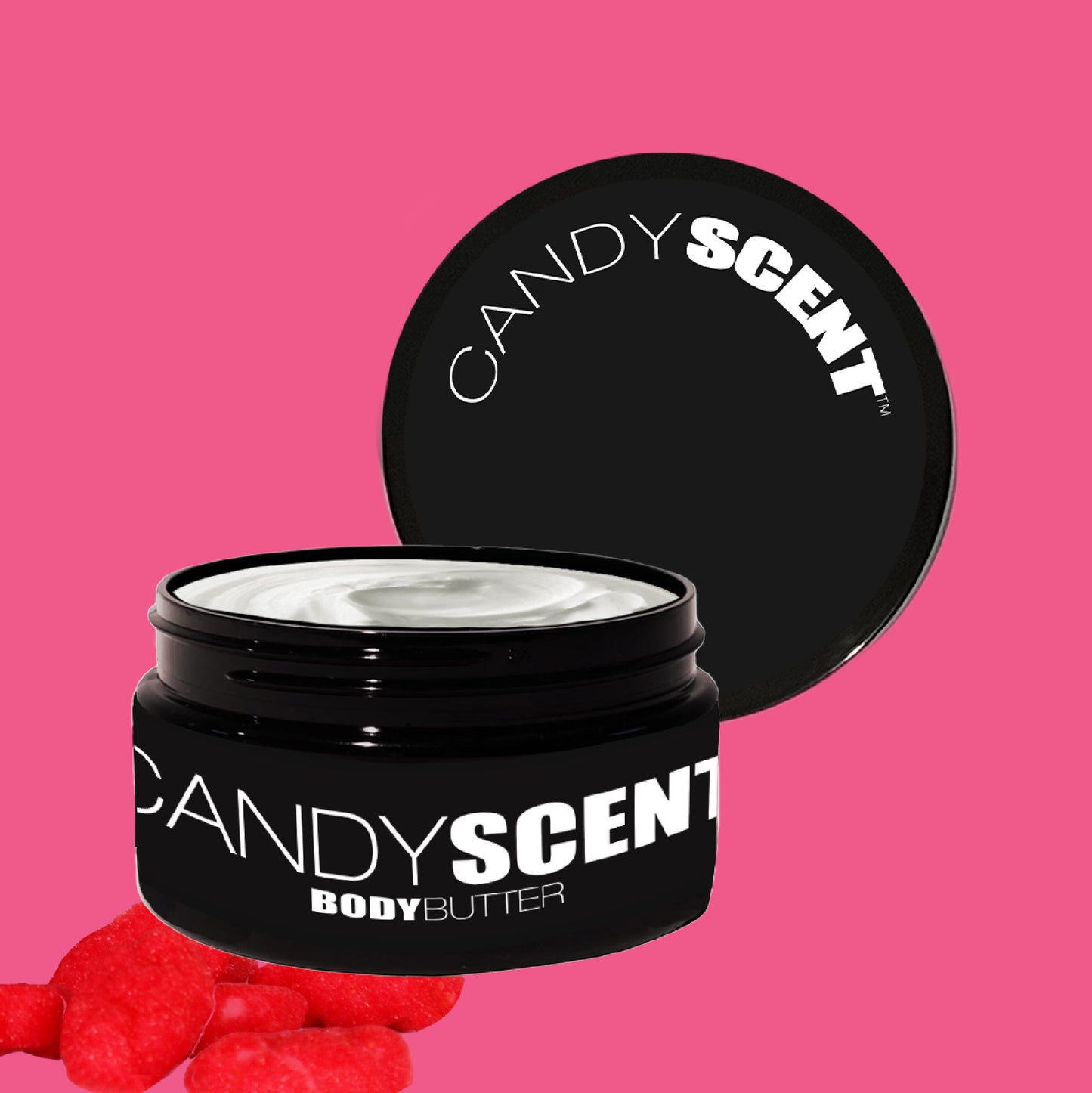 A black container of "Body Butter" by CANDYSCENT™, featuring white text, is open to showcase its creamy texture. The lid rests against the container, suggesting deep hydration and nourishment. A pink background with small red candies scattered at the bottom left complements the scene.