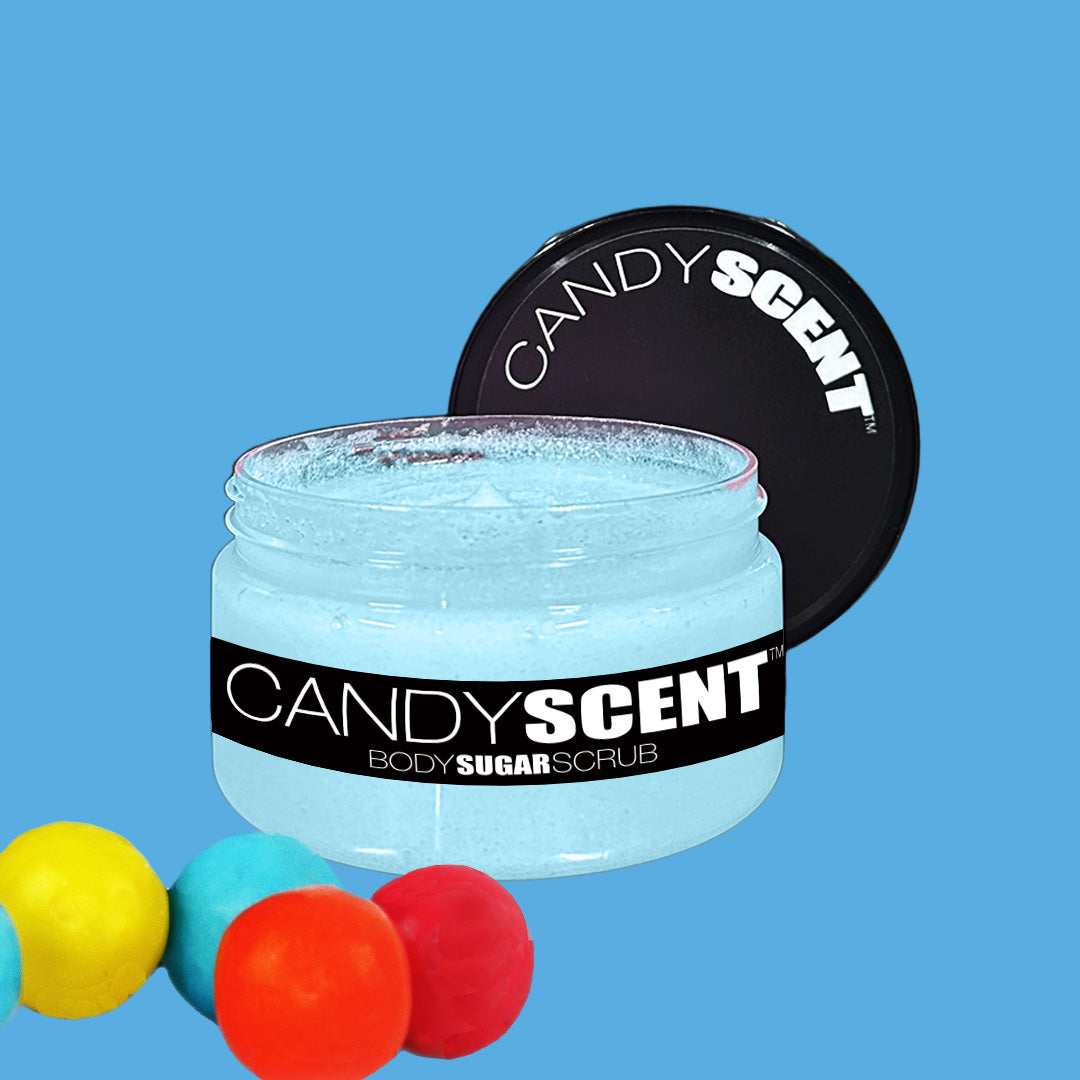 A jar of CANDYSCENT™ Body Sugar Scrub with a black lid sits open, showcasing the light blue exfoliate and hydrate scrub inside. The foreground features colorful gumballs, while the background is a solid light blue hue. This nourishing scrub is infused with hydrating oils to leave your skin smooth and radiant.