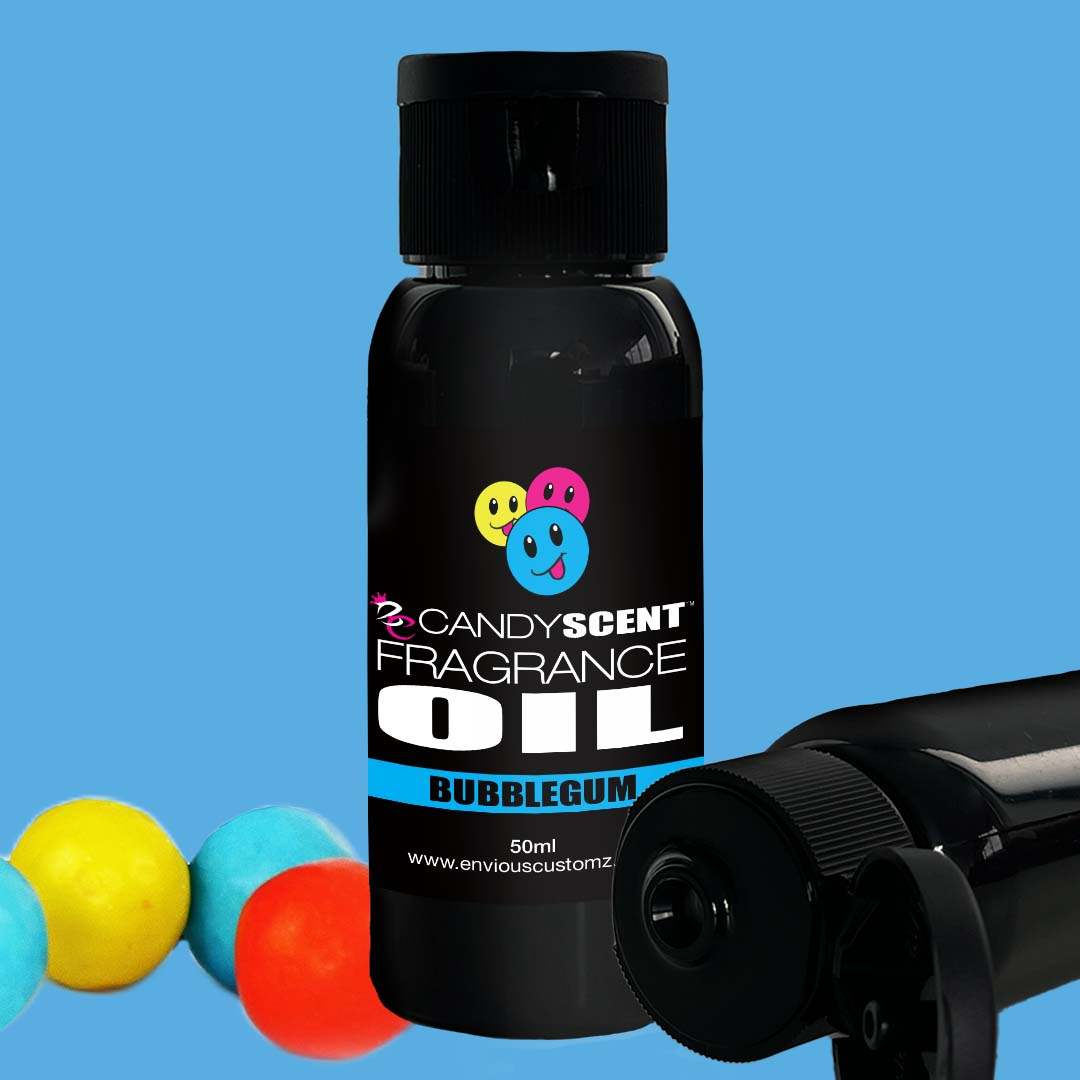 A black 50 ml bottle labeled "Fragrance Oil" by CANDYSCENT™ features a colorful, smiling bubblegum design. The bottle is placed on a blue background with three gumballs (yellow, blue, and red) on the side. Two additional bottles lie horizontally nearby, perfect for your home scent needs or oil burner.