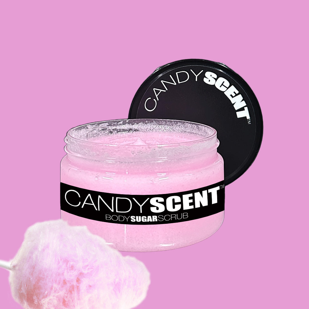 A jar of CANDYSCENT™ Body Sugar Scrub with a black lid is open, displaying the pink scrub within. The jar's label features a black background with white text. Positioned in the foreground is an image of pink cotton candy, while the solid pink background highlights the nourishing oils that exfoliate and hydrate.