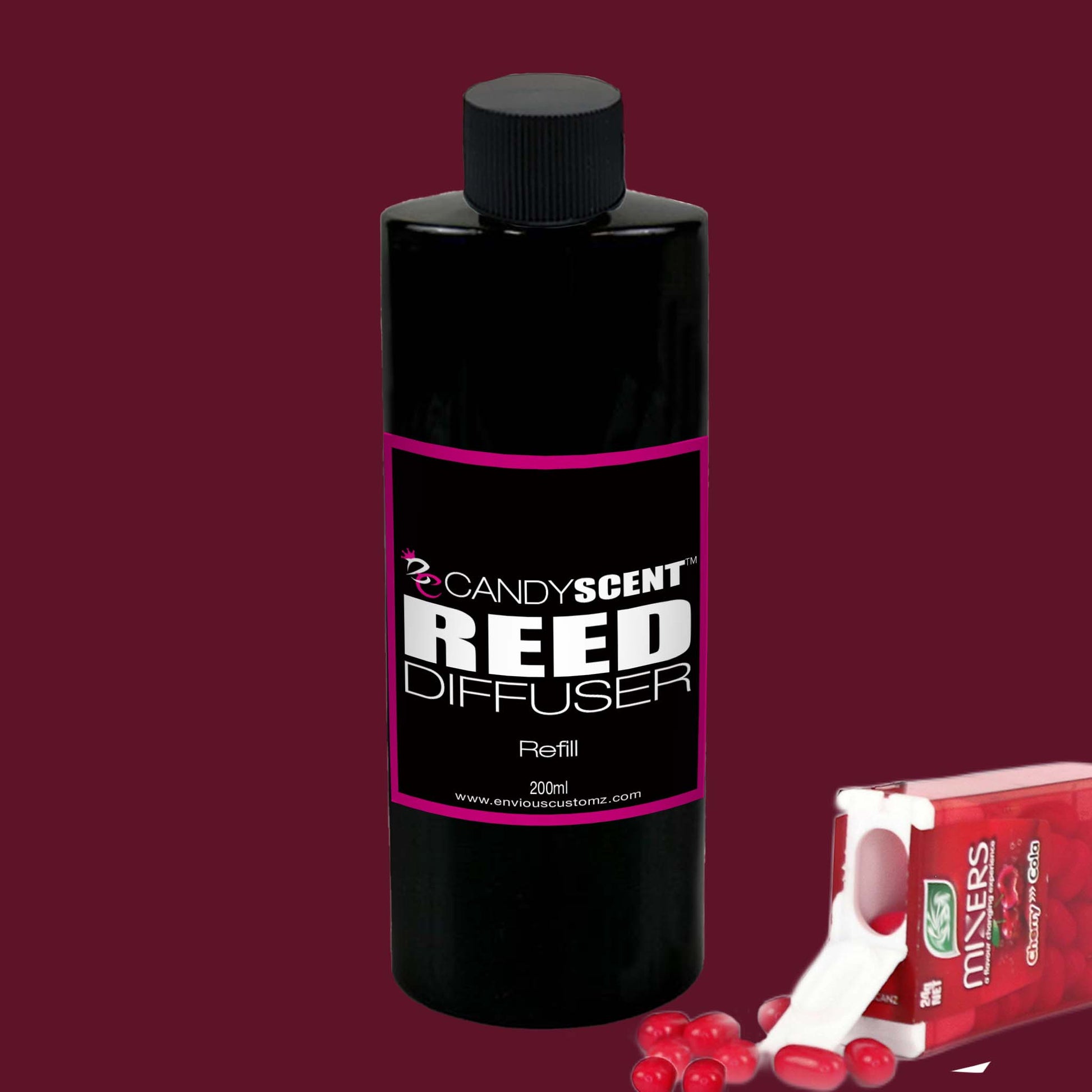 A bottle of CANDYSCENT™ Reed Diffusers & Refills with a black cap and label sits on a red background. The label reads "CANDYSCENT™ Reed Diffuser Refill." Next to it lies a red packet of mints with some red mints spilling out. This Australian made diffuser promises a long-lasting fragrance.