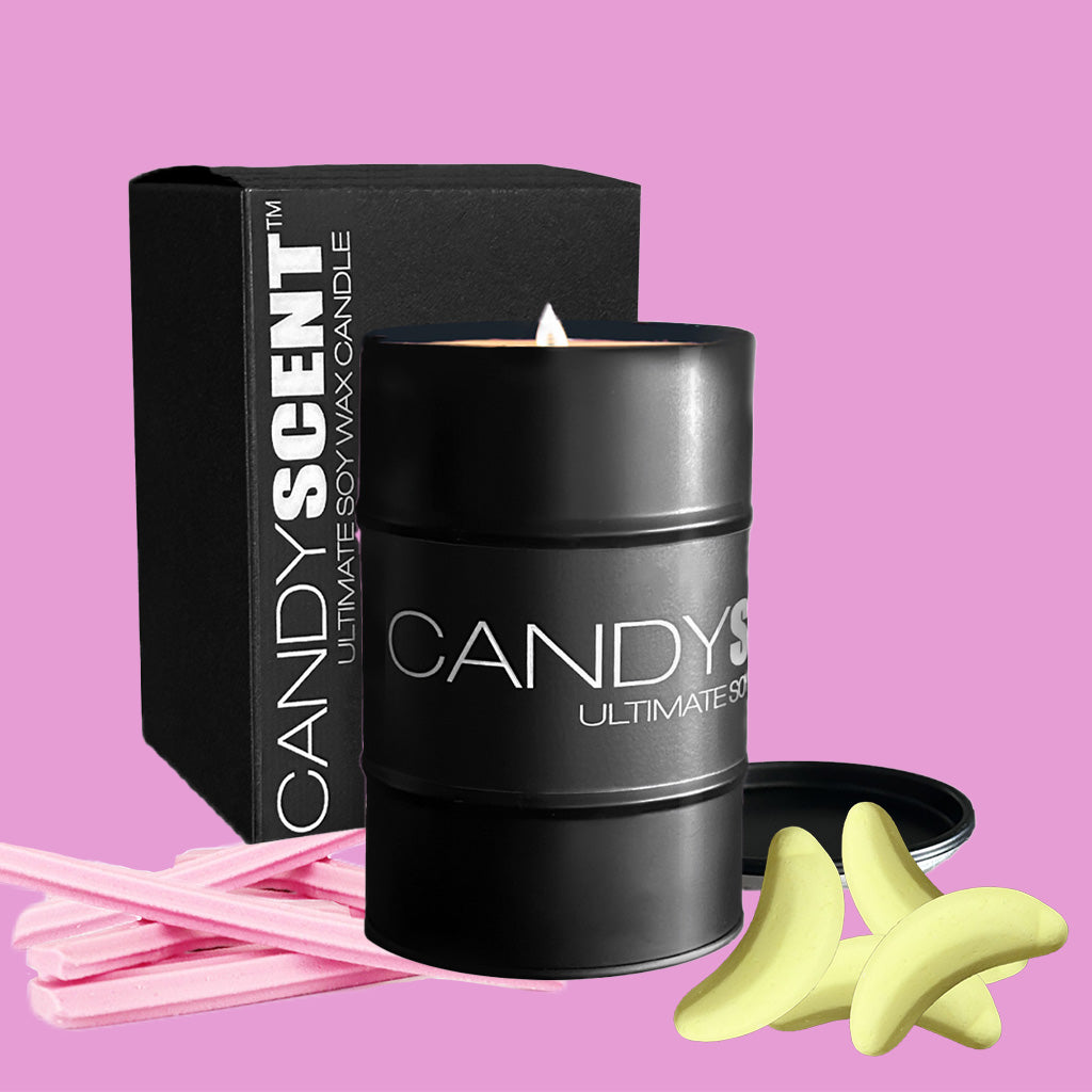 A black cylindrical candle labeled "CANDYSCENT™ Soy Wax Candle Tin" with a matching black box. The candle is lit, and beside it are pink sticks and two yellow banana-shaped items, all set against a light purple background.