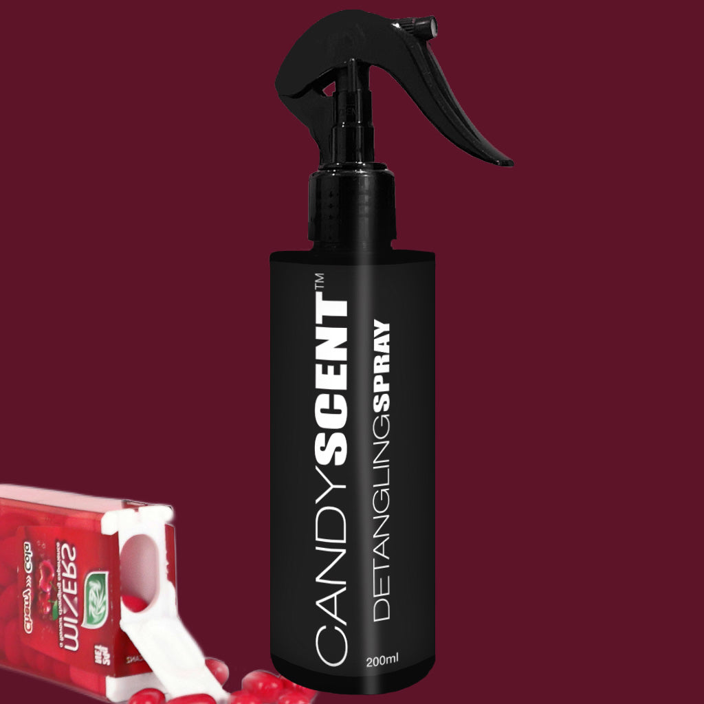 A black spray bottle of CANDYSCENT™ Hair Detangling Spray, enriched with jojoba oil and aloe vera, is set against a dark maroon background. Beside it, a red package of Tic Tac mint candies is partially open, exposing several red mints spilling out.