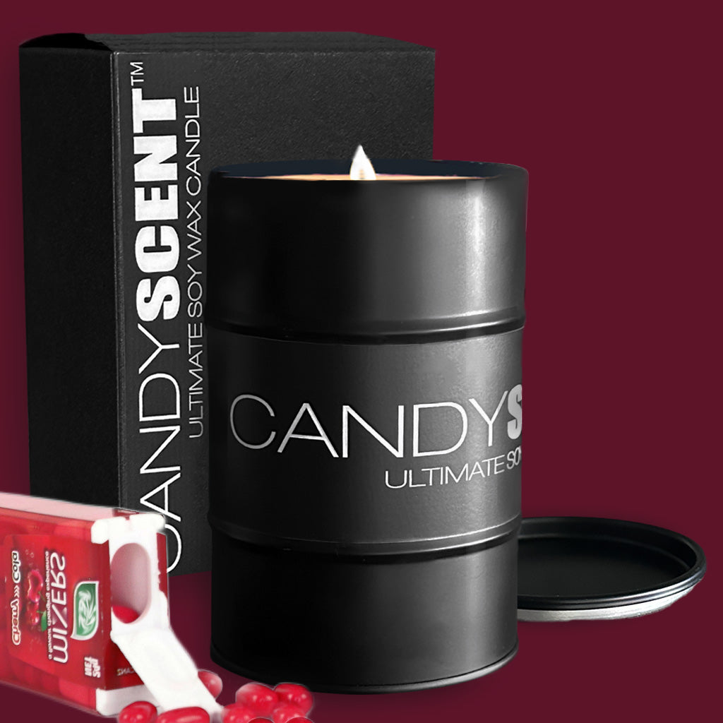 A lit black "CANDYSCENT™ Soy Wax Candle Tin" sits in front of its black packaging box on a maroon background. Nearby, a small pack of Tic Tac candies and some loose Tic Tac candies are strategically placed.