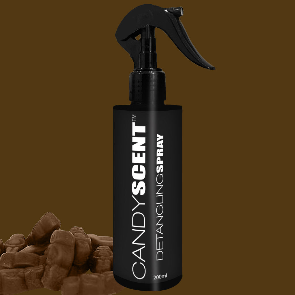 A black spray bottle labeled "CANDYSCENT™ Hair Detangling Spray" with a trigger nozzle is centered on a brown background. Infused with jojoba oil, the 200ml bottle promises smooth and shiny hair. At the bottom left, several pieces of candy add a playful touch.