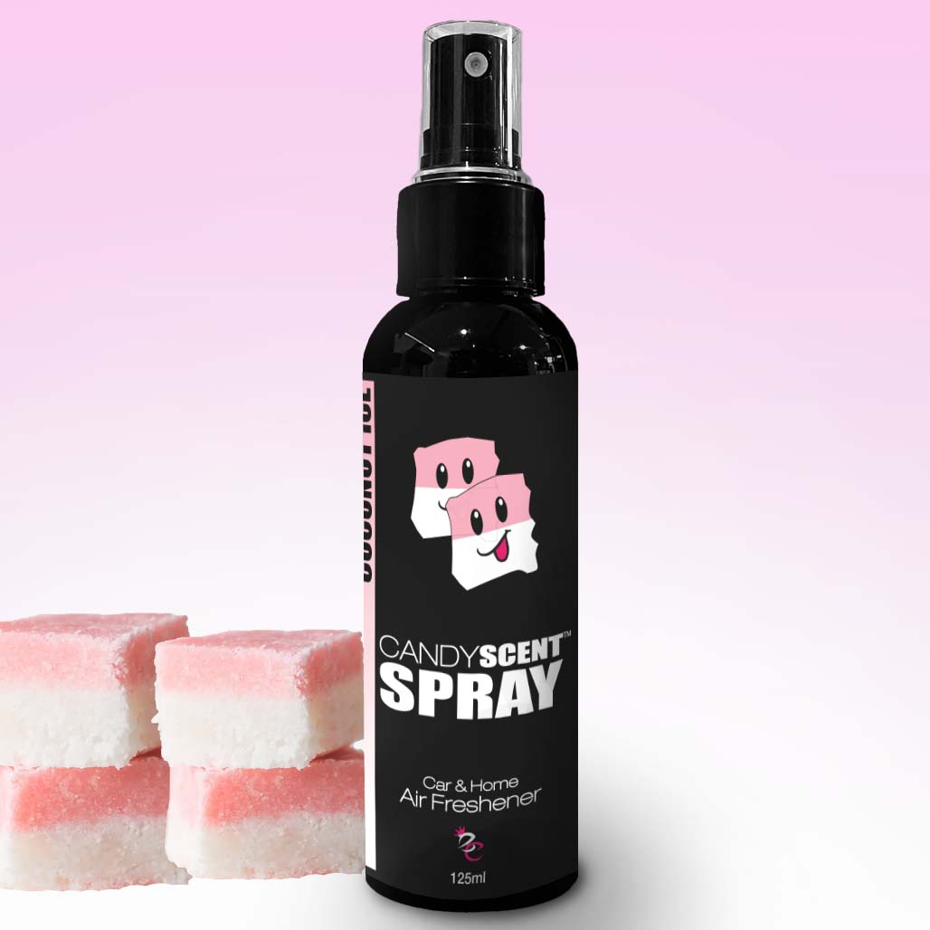 A black spray bottle labeled "CANDYSCENT™ Car & Home Scent Sprays" for air freshening is showcased against a gradient pink backdrop. The bottle displays a playful cartoon image of smiling candy cubes and guarantees to eliminate odors. Nearby, three pink and white layered candy pieces add an extra touch of charm.