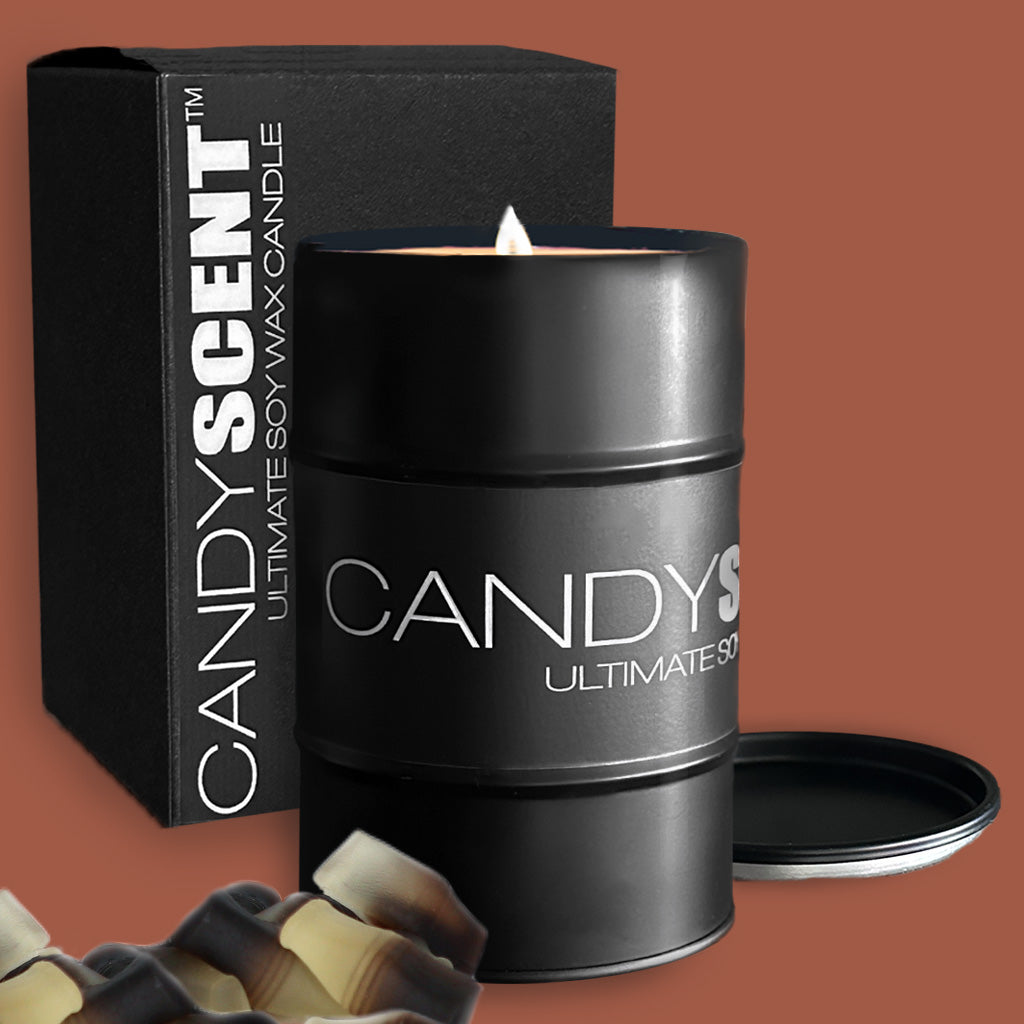 A burning black candle labeled "CANDYSCENT™ Soy Wax Candle Tin" stands beside its sleek black packaging box, displaying the same branding. Near the soy wax candle, several small pieces of candy are partially visible in the corner.