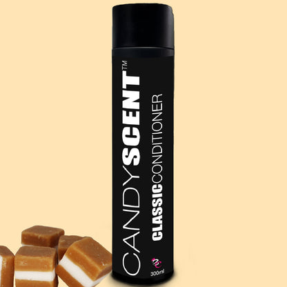 A tall, cylindrical black bottle of CANDYSCENT™ Classic Conditioner stands upright against a light yellow background. The 300 ml bottle is surrounded by several pieces of caramel candy chunks, hinting at its sweet aroma with nourishing macadamia oil.