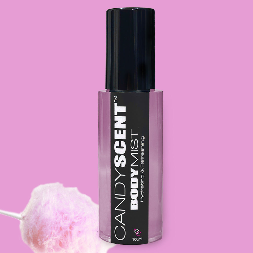 A bottle of Hydrating Body Mist by CANDYSCENT™ against a pink background. The cylindrical bottle with a black cap and label is infused with nourishing ingredients like witch hazel. It is described as "Hydrating & Refreshing" and contains 100ml of product. A fluffy piece of pink cotton candy rests at the bottom left.