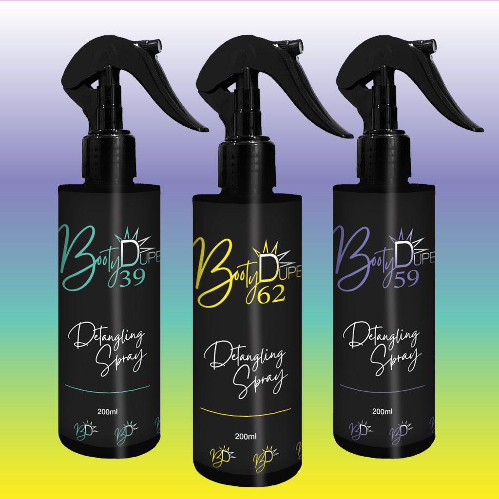 The image showcases three black bottles of "BOOTY DUPE Hair Detangling Spray" with trigger tops, uniquely numbered 39, 62, and 59. The gradient backdrop blends green, blue, yellow, and purple. Each bottle contains 200ml of product enriched with Aloe Vera and Jojoba Oil, suitable for all hair types.