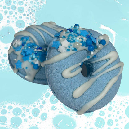 Two CANDYSCENT™ Bath Bombs, shaped like blue donuts and adorned with white glaze alongside a medley of blue and white sprinkles—including tiny stars and pearls—set against a bubbly blue background imbued with sweet scents.