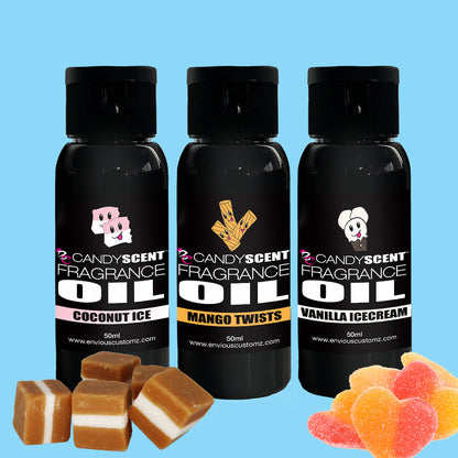 Three bottles of CANDYSCENT™ Fragrance Oil, each 50ml, arranged against a light blue background. The scents include Coconut Ice, Mango Twists, and Vanilla Ice Cream. Below the bottles are square-shaped candies and sugar-coated gummy hearts—ideal for your oil burner or enhancing your home's aroma.