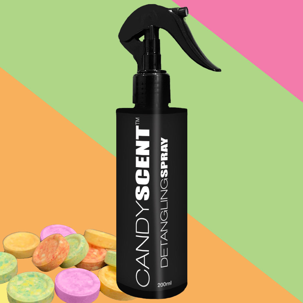 A black spray bottle labeled "CANDYSCENT™ Hair Detangling Spray" with aloe vera and jojoba oil, featuring a 200ml capacity, stands against a colorful background divided into sections of pink, lime green, and orange. Candy-colored round tablets are scattered at the bottom left corner of the image.