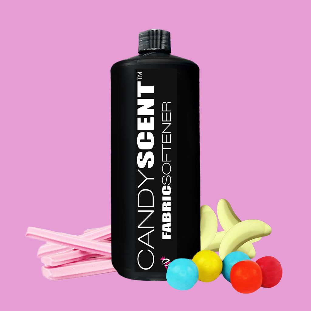 A black bottle of CANDYSCENT™ Fabric Softener stands out against a pink background, ensuring a static-free experience. It is accompanied by candy-shaped objects such as pink gum sticks, colorful round candies, and yellow banana sweets, reflecting its sweet fragrance.