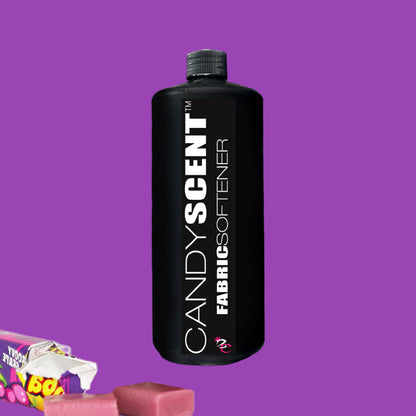 A black bottle labeled "Fabric Softener" from CANDYSCENT™ takes center stage against a purple background, offering a static-free experience. Two unwrapped pink candies and a candy wrapper enhance the charm in the bottom left corner.