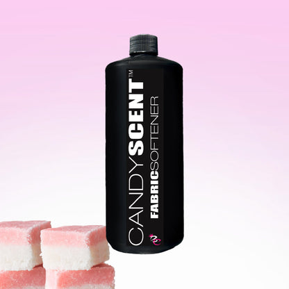 A bottle of CANDYSCENT™ Fabric Softener featuring a black label is set against a pink gradient background, offering a static-free experience. In the lower left corner, three pink and white cubes resembling marshmallows add a playful touch.