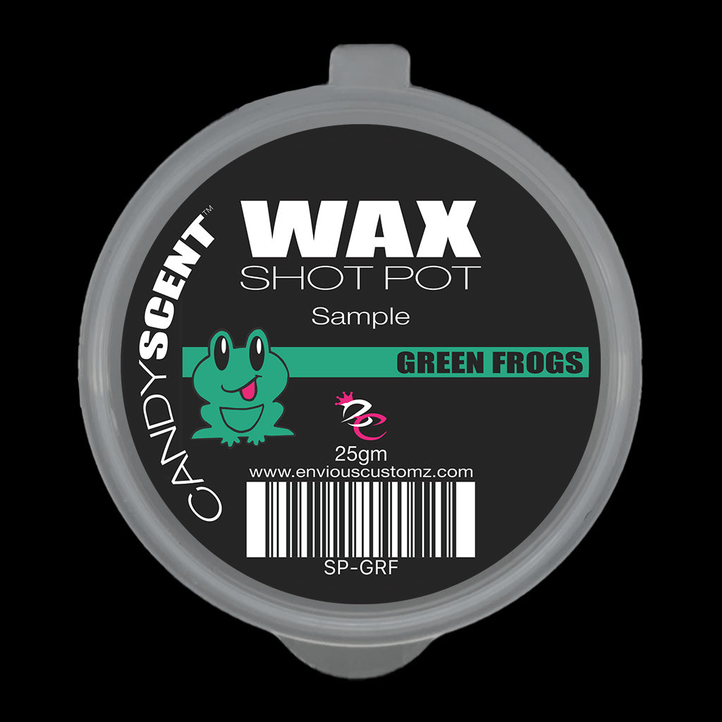 A circular container branded with "CANDYSCENT™'s Wax Melts" and labeled as a sample of "GREEN FROGS" showcases a cartoon frog on its black lid. Ideal for home fragrance lovers, this 25g wax melt comes with a barcode and website address for further information.