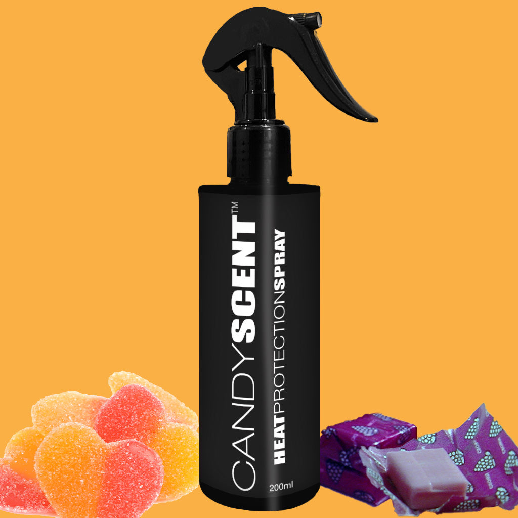 Positioned against a solid orange backdrop is a black bottle of CANDYSCENT™ Heat Protection Spray, complete with a spray nozzle. Heart-shaped gummy candies and two wrapped pieces of taffy surround the bottle, highlighting its promise of salon-quality results.