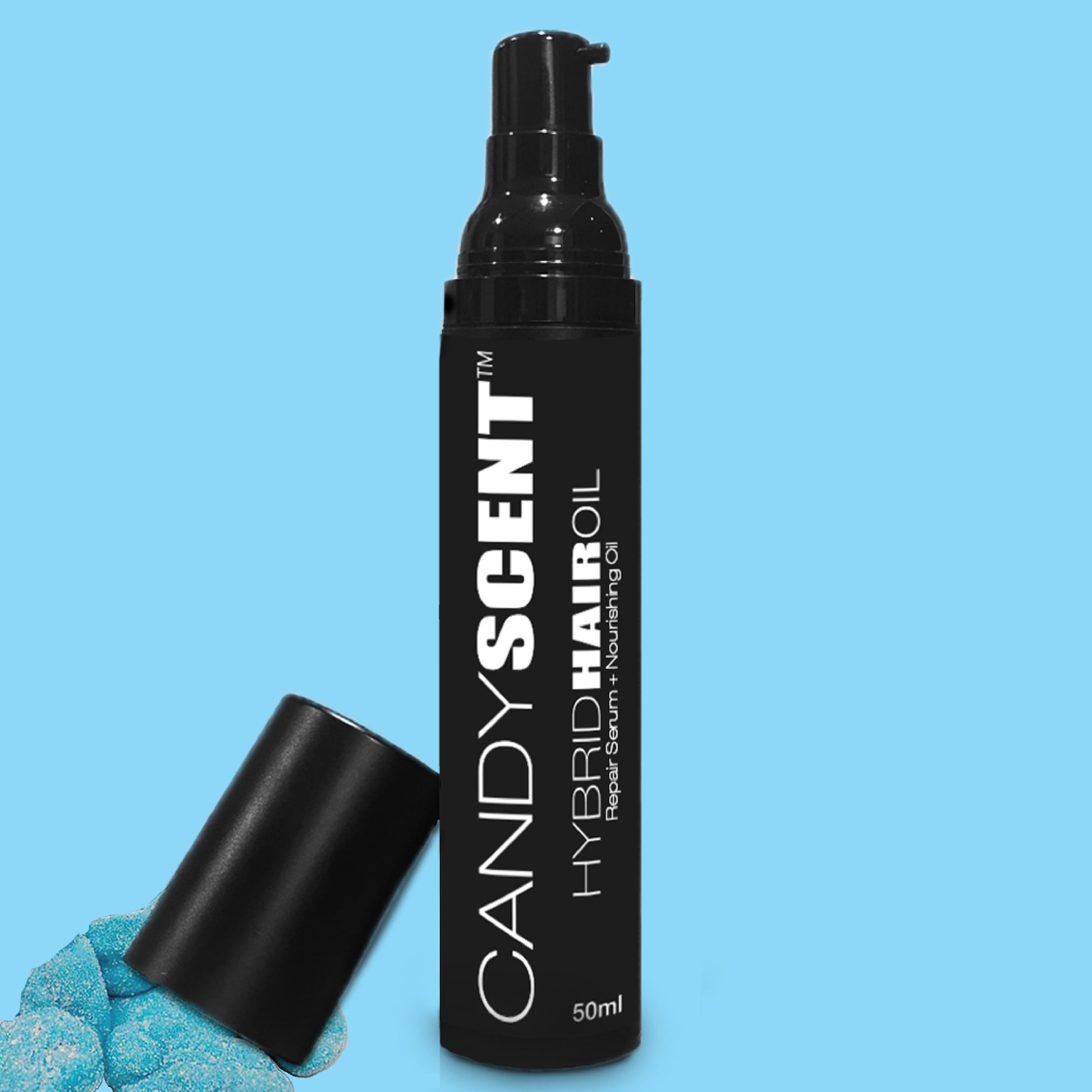 A black pump bottle labeled "CANDYSCENT™ Hybrid Hair Oil" is set against a blue background. The bottle's cap is off and placed nearby, next to a few blue, sugar-coated gummy candies.