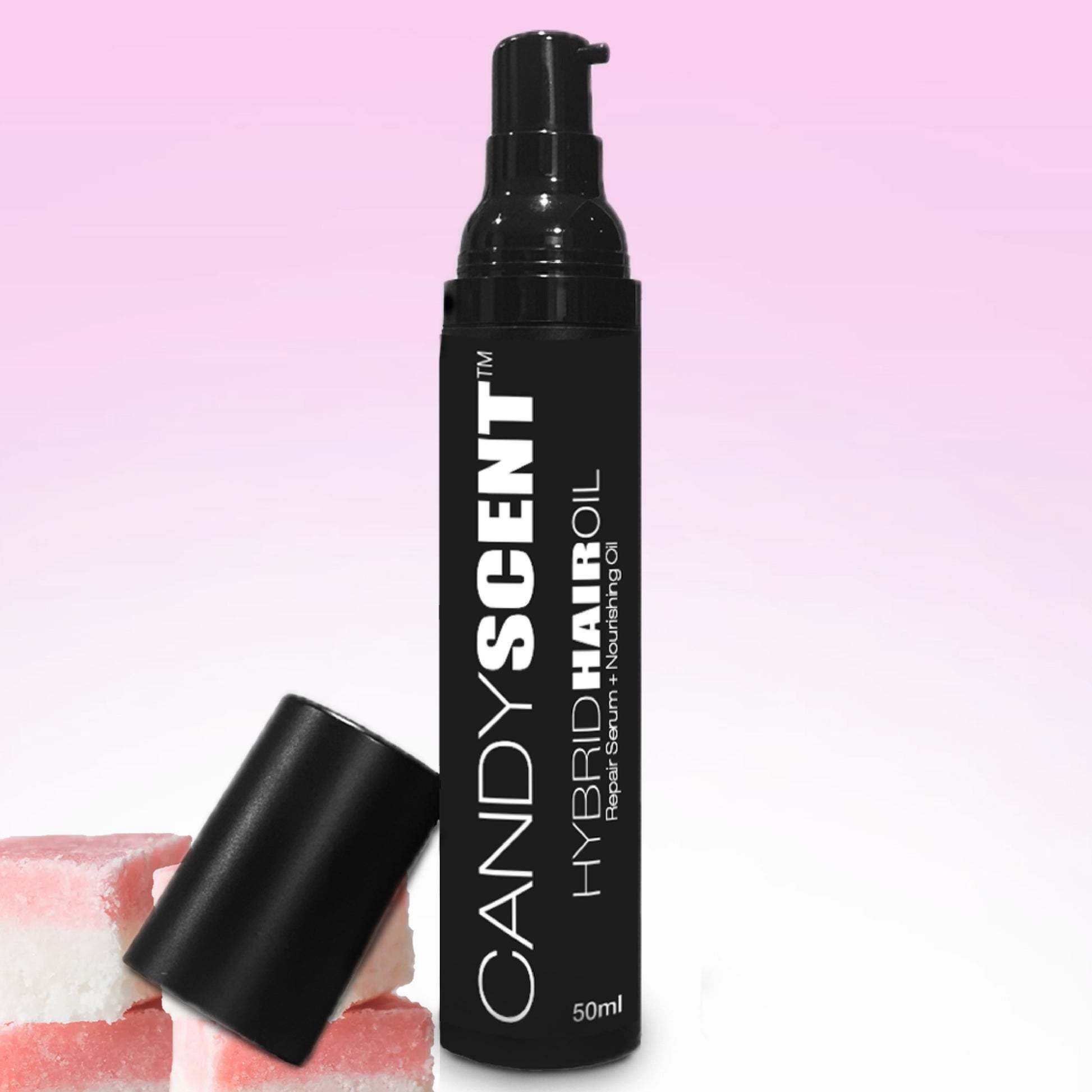 A 50ml black bottle of CANDYSCENT™ Hybrid Hair Oil stands against a pink gradient background. The bottle features a pump dispenser with an unattached black cap beside it. Three pieces of pink and white candy are positioned near the base, highlighting this nourishing hair oil.