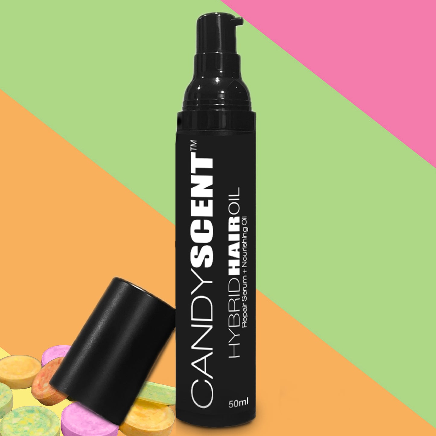 A black bottle of CANDYSCENT™ Hybrid Hair Oil, equipped with a pump dispenser and a detached cap, is set against a vibrant, diagonal multi-colored background. In the corner, an assortment of pastel-colored round candies adds a playful touch. The 50ml bottle promises to rejuvenate hair with every use.