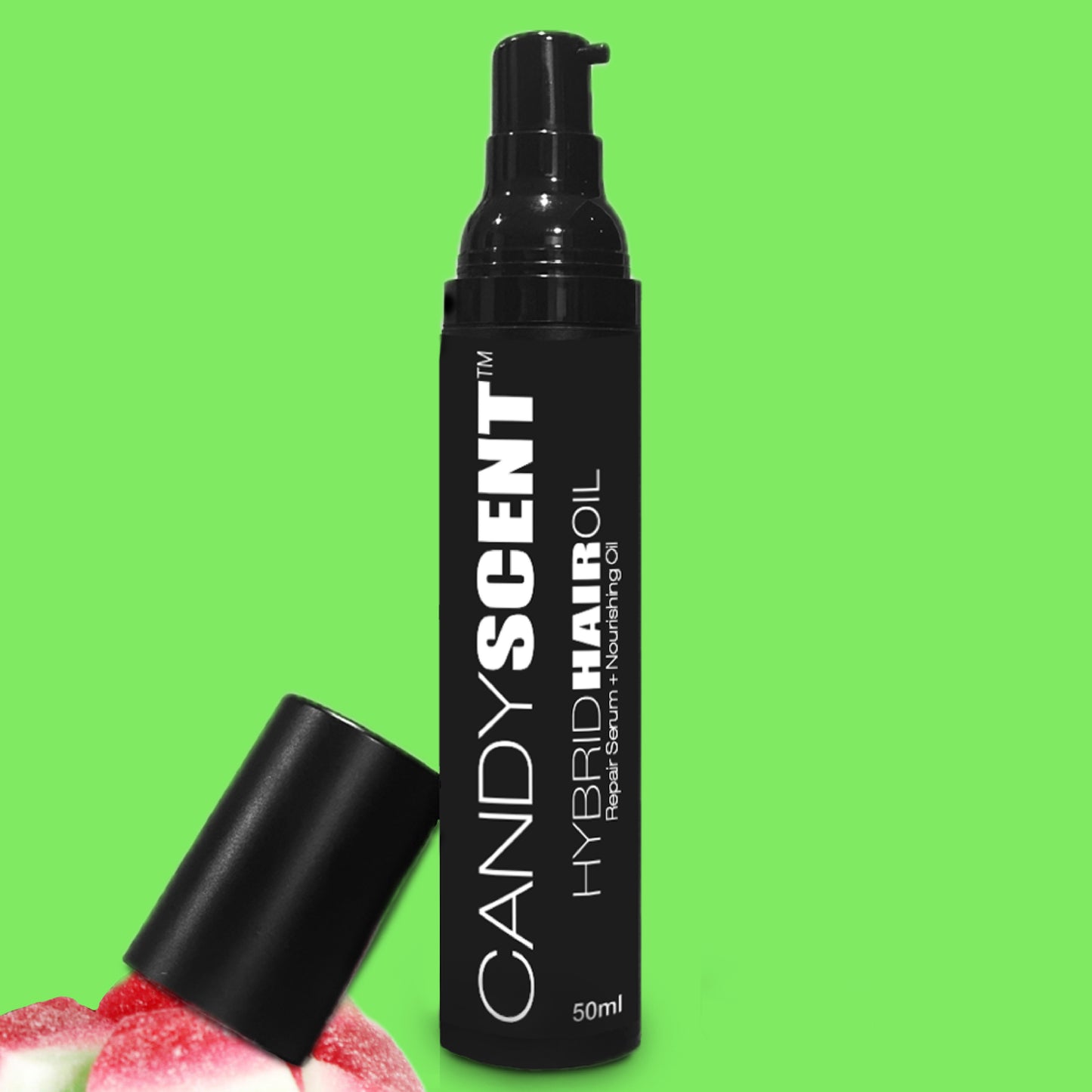 A black bottle labeled "Hybrid Hair Oil" from CANDYSCENT™ stands against a bright green background. The bottle, which includes a pump dispenser and its cap beside it, is surrounded by pink and white candy-like objects in the bottom left corner.