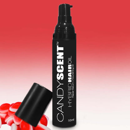 A black bottle labeled "Hybrid Hair Oil" by CANDYSCENT™, with a pump dispenser, stands against a gradient red background. The bottle's cap lies sideways next to several red and white lollipops, accentuating the nourishing hair oil within.