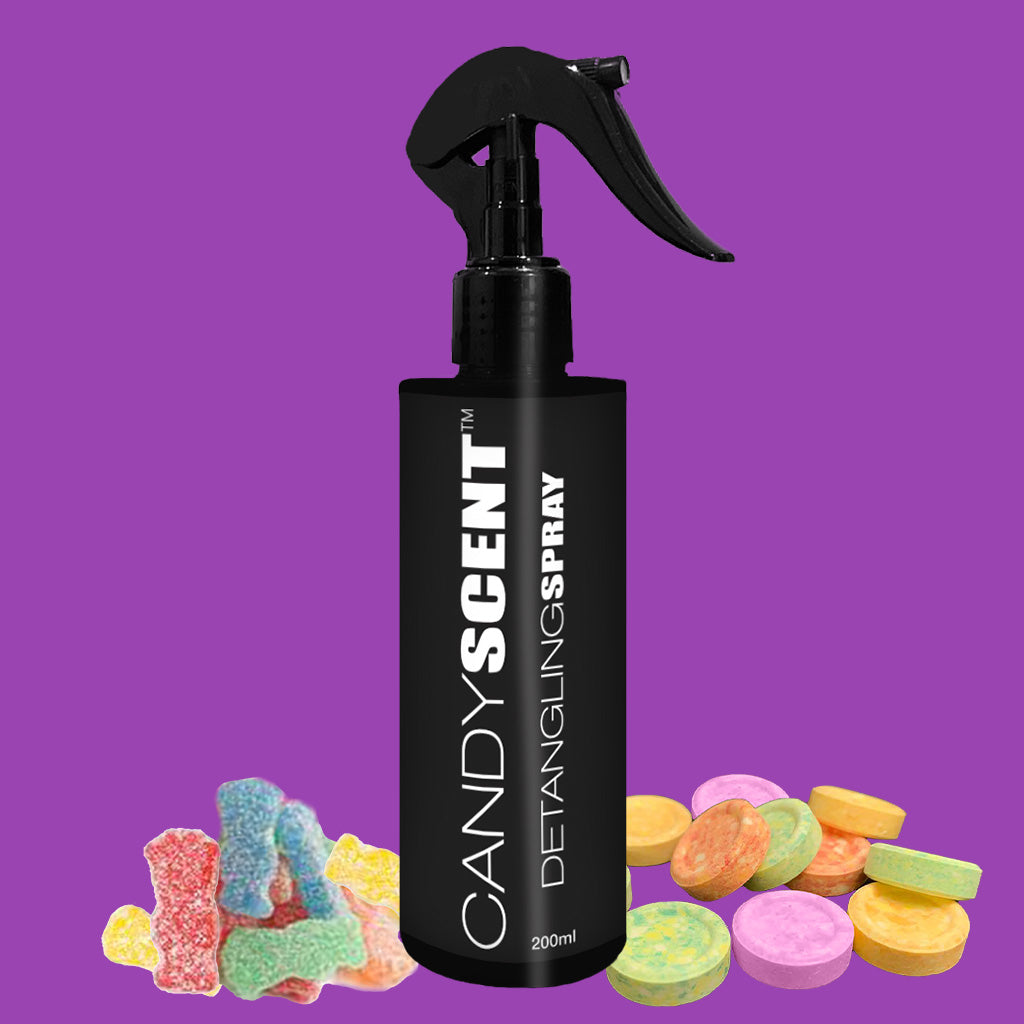 A black spray bottle labeled "CANDYSCENT™ Hair Detangling Spray, 200ml" is set against a purple background. The scene is adorned with colorful candy-like items, including gummy bears in shades of yellow, red, and blue, as well as round discs in pastel colors. The spray features nourishing jojoba oil and soothing aloe vera.