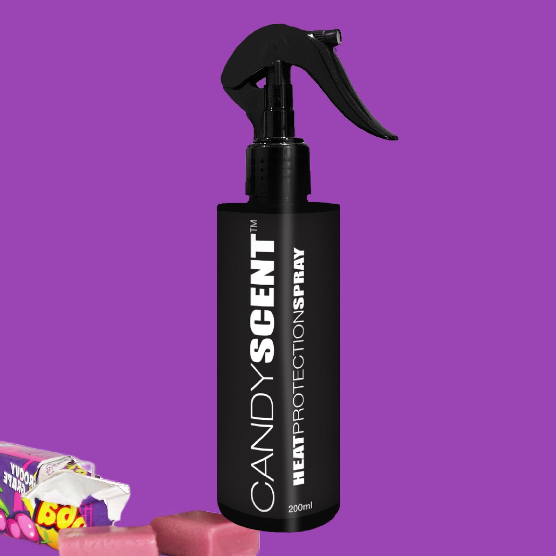 A black bottle of CANDYSCENT™ Heat Protection Spray, complete with a nozzle, is set against a vibrant purple backdrop. Surrounding it, pink candy pieces and gum in colorful wrappers create a playful atmosphere, representing salon-quality results in both appearance and performance.