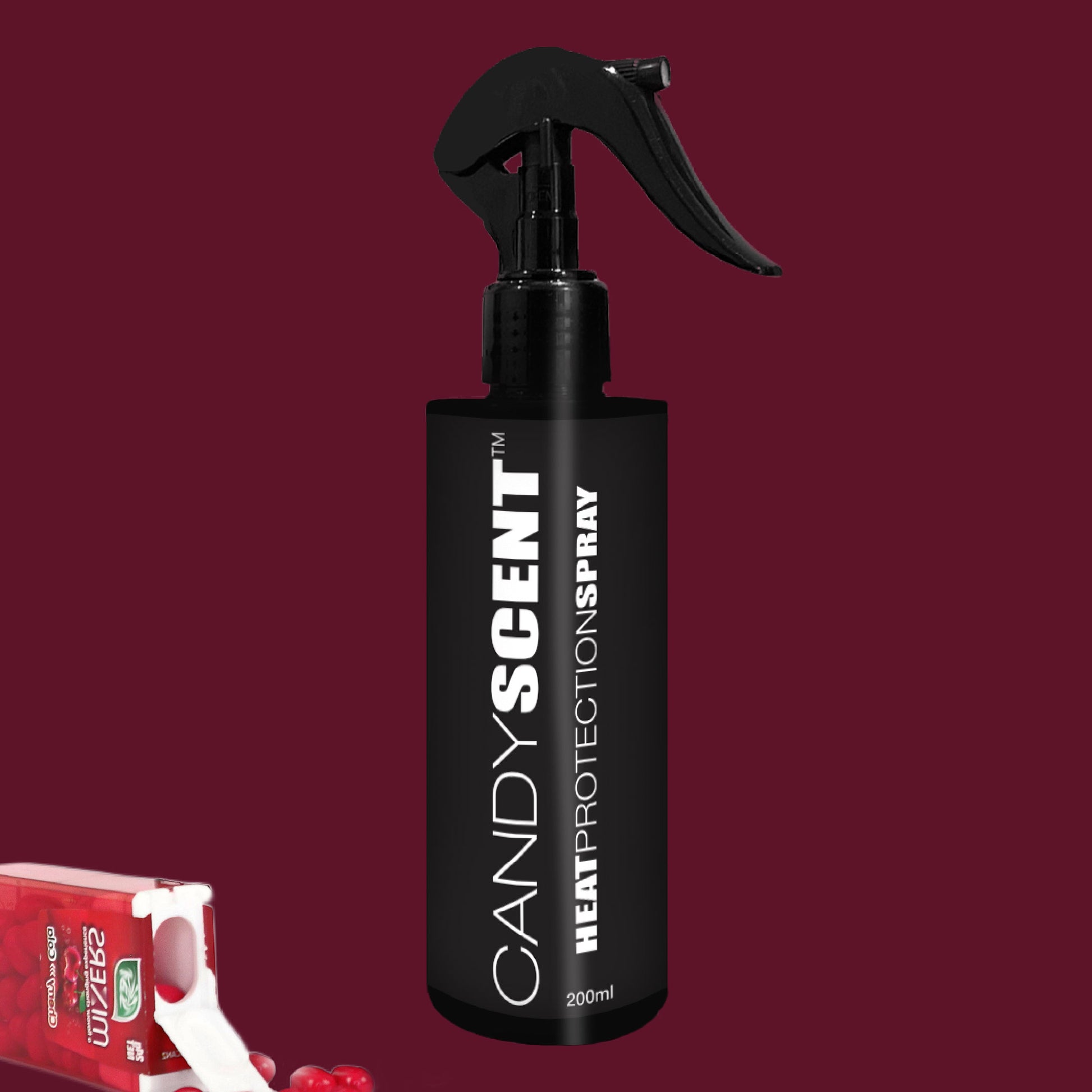 A black CANDYSCENT™ Heat Protection Spray bottle, equipped with a trigger nozzle, is set against a red-maroon background. The scene features a partially visible red and white carton along with small red spheres, alluding to salon-quality results.